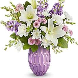 White lilies and purple flowers arranged in a lavender vase