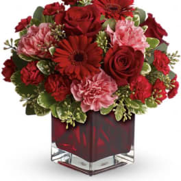 Red and pink flower arrangement in a square glass vase