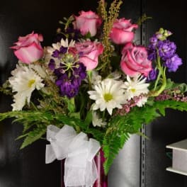 Pink roses and white daisies in a red vase with a white bow