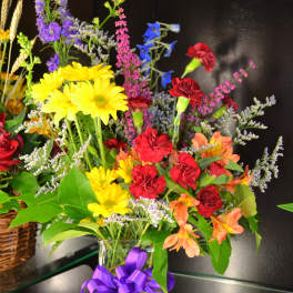 Mixed bouquet of yellow daisies, red carnations, and orange alstroemeria in a glass vase