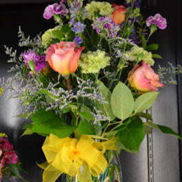 Mixed bouquet of roses and purple flowers in a glass vase with a yellow bow
