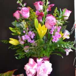 Pink roses and yellow lilies in a glass vase with a pink ribbon