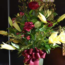 Bouquet of yellow lilies and burgundy carnations in a vase with a red ribbon