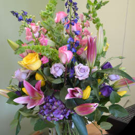 Mixed bouquet of roses, lilies, hydrangea, and blue flowers in a glass vase