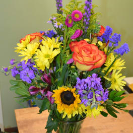 Colorful mixed bouquet in a clear glass vase with a sunflower and orange rose