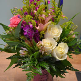 Mixed bouquet of white roses, pink lilies, and purple flowers in a pink vase