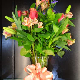 Bouquet of pink lilies and purple filler flowers in a glass vase with a peach ribbon