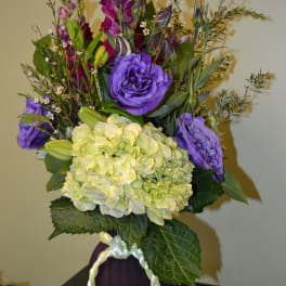 Purple and yellow floral arrangement in a dark vase with a braided ribbon handle