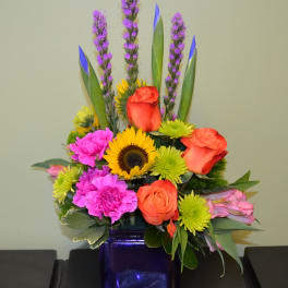 Colorful mixed bouquet in a purple glass vase with roses and sunflowers