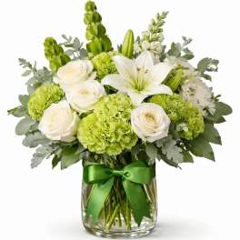 White lilies and roses with green blooms in a glass vase tied with a green ribbon