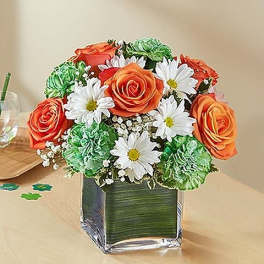 Bouquet of orange roses, white daisies, and green carnations in a square glass vase