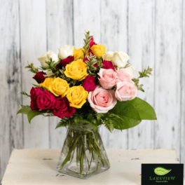 Mixed bouquet of red, yellow, white, and pink roses in a clear glass vase