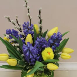 Spring arrangement of yellow tulips and blue hyacinths with pussy willow branches and a small yellow chick decoration