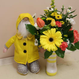 Yellow-clad doll beside a mixed bouquet in a white vase