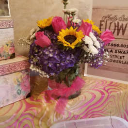 Bouquet of pink roses, sunflowers, and purple hydrangeas in a glass vase