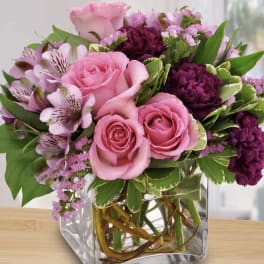Pink roses and purple flowers arranged in a clear square vase