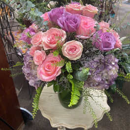 Arrangement of pink and lavender roses with purple hydrangeas in a green glass vase on a small table