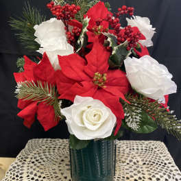 Red and white floral arrangement in a green vase with pine accents