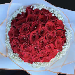 Round bouquet of red roses with pearl centers, edged with small white flowers in white wrapping.