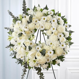 White floral wreath on a black easel with roses and daisies