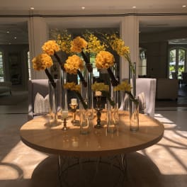 Yellow rose arrangements in tall glass vases on a round table with candles