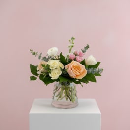 Mixed roses in a clear glass vase on a white pedestal