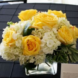 Yellow roses and white hydrangeas in a clear square vase