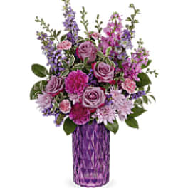 Purple and pink mixed flower arrangement with roses and carnations in a tall purple glass vase