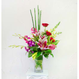 Tropical bouquet with red roses, pink lilies, and purple orchids in a glass vase