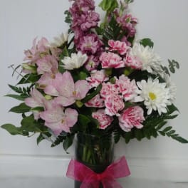 Pink and white mixed flower arrangement in a clear glass vase with a pink bow