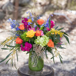 Colorful bouquet of roses, blue flowers, and hydrangea in a green vase