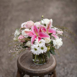 Pink lilies, roses, and white daisies arranged in a glass vase