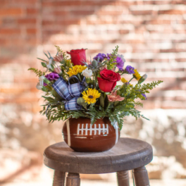 Bouquet of red roses and mixed flowers in a football-shaped vase