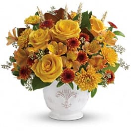 Low round arrangement of yellow roses and orange mums in a white ceramic bowl