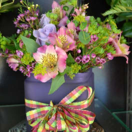 Pink and lavender flowers in a purple container with a plaid ribbon