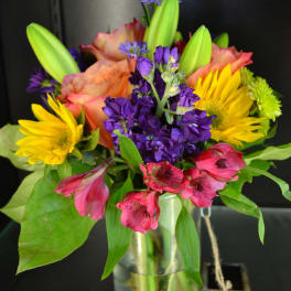 Colorful bouquet of lilies, sunflowers, and purple flowers in a glass vase
