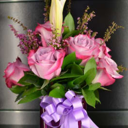 Pink roses and a white lily in a purple vase with a ribbon