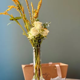 White roses in a clear glass vase with a soap bar gift box beside it.
