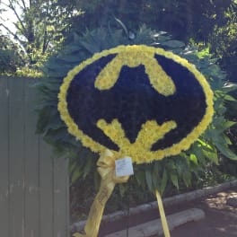Batman logo floral wreath on a stand with yellow and dark flowers
