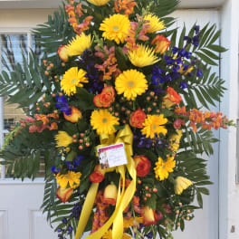 Large standing spray of yellow, orange, and blue flowers with a yellow ribbon