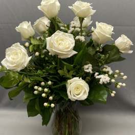 Tall arrangement of white roses and white filler flowers in a clear glass vase