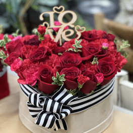 Heart-shaped box of red roses and carnations with a "Love" topper