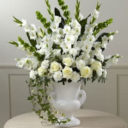 White flowers arranged in a white urn vase with trailing ivy.