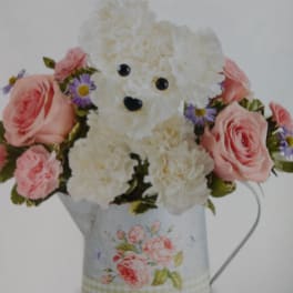 White teddy bear surrounded by pink roses and purple flowers in a floral tin