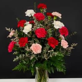 Tall bouquet of red, white, and pink carnations in a clear glass vase