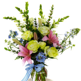 Bouquet of pink lilies and pale yellow roses in a glass vase with a blue ribbon