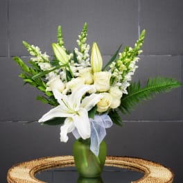 White lilies and roses in a green vase with a sheer ribbon