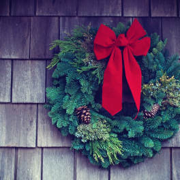 Evergreen wreath with a red bow and pinecones on a shingled wall