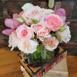 Low arrangement of pale pink roses and white calla lilies in a glass vase on stacked vintage books.