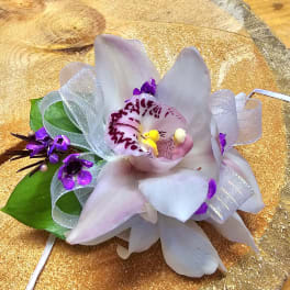 Small orchid corsage with white ribbon and green leaves